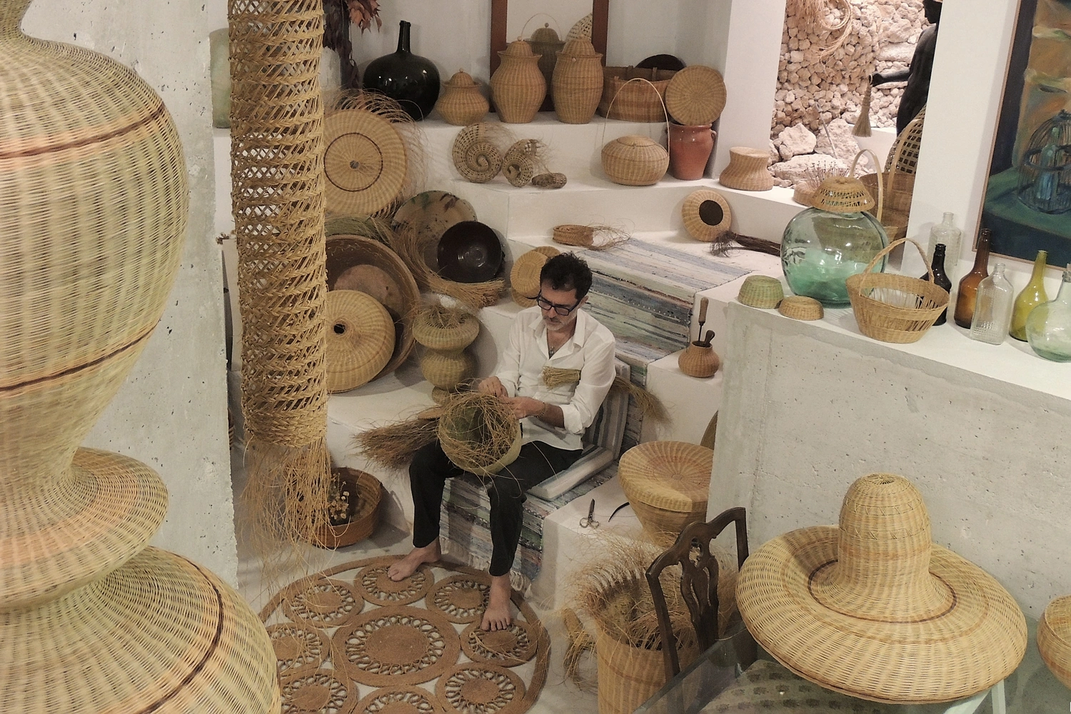 Joaquín sentado trabajando entre sus formas tejidas, herramientas y materiales en el taller real
